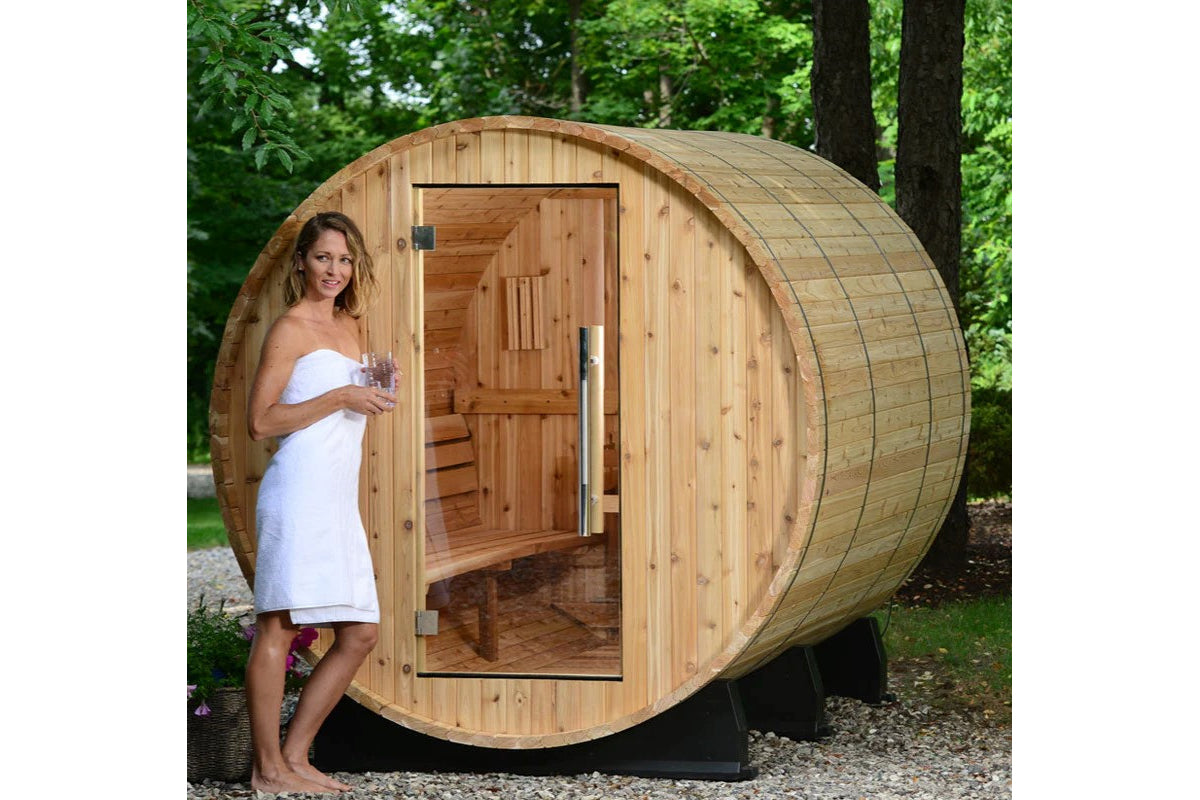 Wooden barrel sauna with curved cedar exterior, open door showing interior benches, model in white towel standing outside, su
