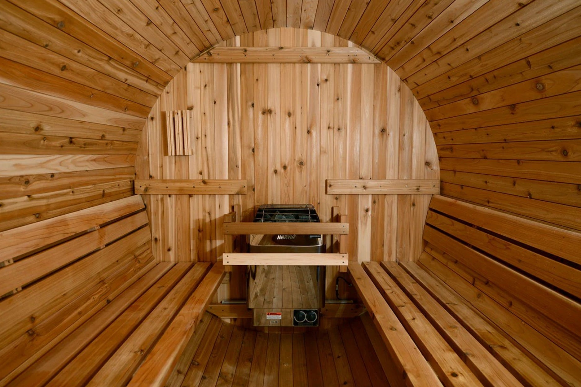 Interior view of barrel sauna with light wood construction, curved ceiling, wooden benches on both sides, and sauna heater wi
