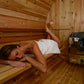 Woman relaxing on wooden bench inside cedar sauna with stainless steel heater stove