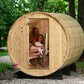 Cylindrical wooden barrel sauna with natural pine construction, open door showing two people inside, set in wooded garden set