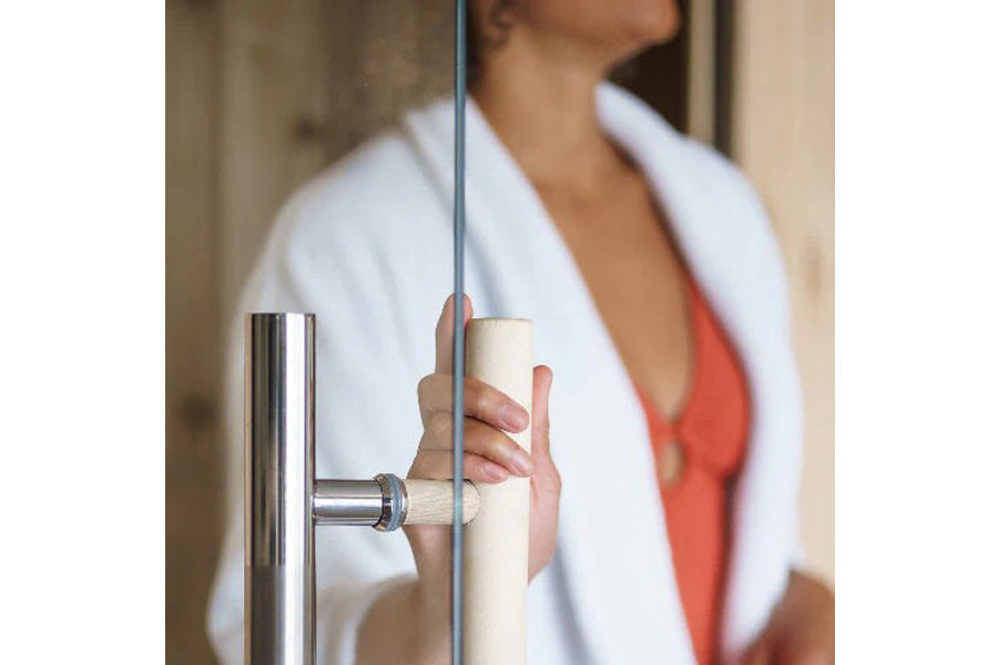 Polished stainless steel door handle on glass sauna door, model worn by person in white robe and coral top