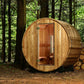 Cylindrical wooden barrel sauna with natural wood exterior and open wooden door showing interior, in forest setting with stac