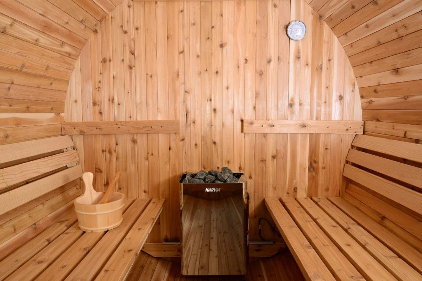 Interior view of wooden sauna with two benches on either side, Harvia heater with stones in center, wooden bucket with ladle 