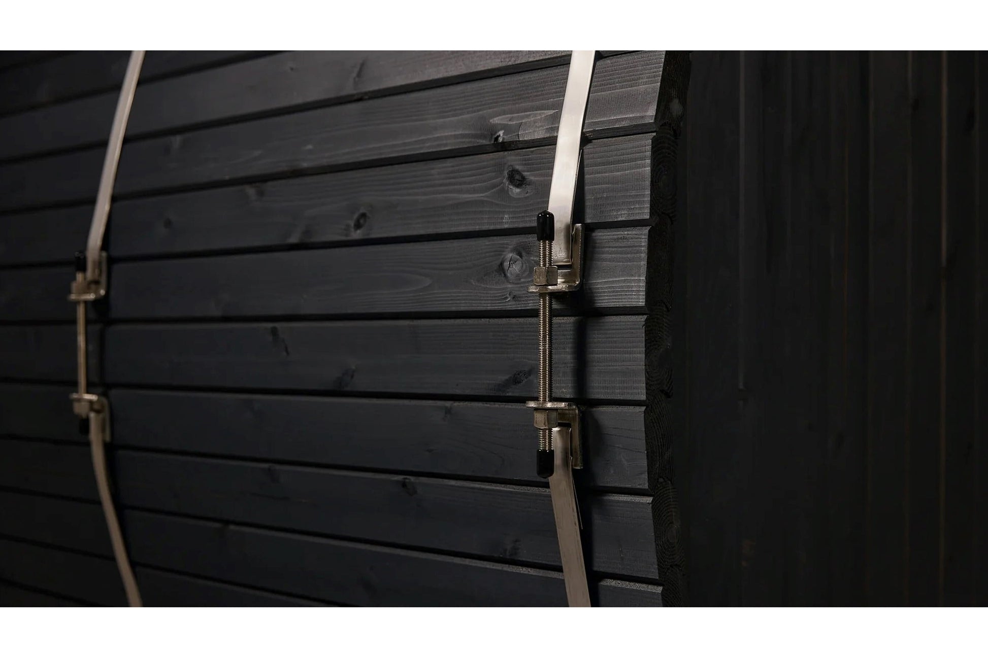 Black wooden sauna barrel with horizontal planks, metal hinged door latch, and rope detail on the side