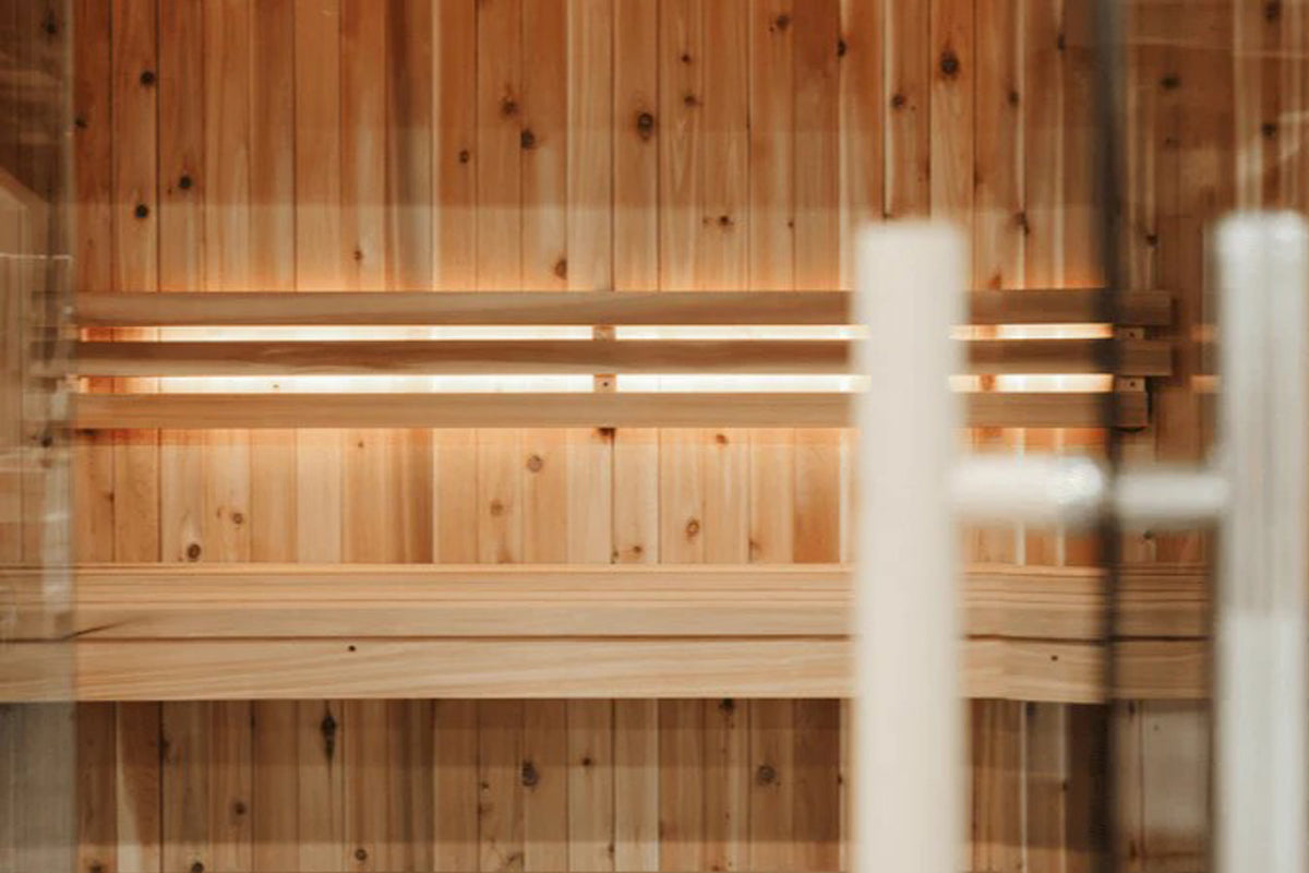Wooden sauna interior with light benches and infrared heating elements mounted on knotty pine walls