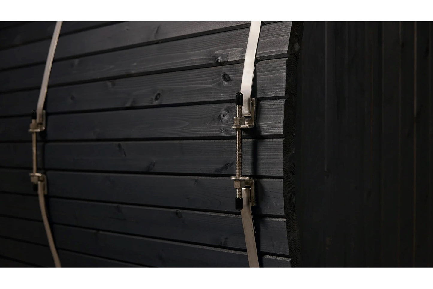 Black wood barrel sauna exterior with horizontal shiplap siding and metal straps with silver buckle closures