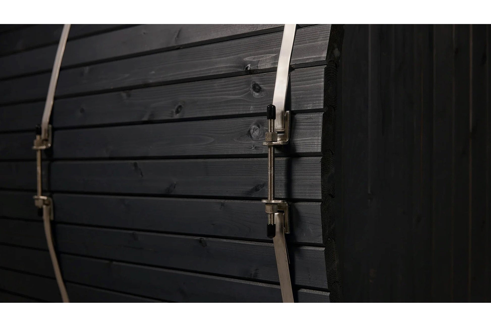Black wood barrel sauna exterior with horizontal shiplap siding and metal straps with silver buckle closures