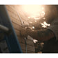 Man in gray shirt installing stainless steel bands on wooden barrel sauna in sunlight