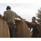 Two men assembling a wooden barrel sauna outdoors, with one wearing a beige shirt and the other in dark clothing and sunglass