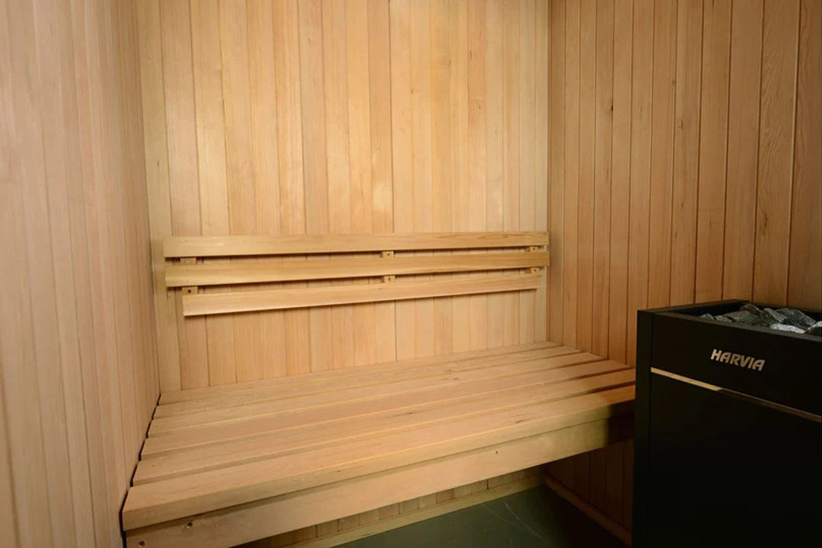 Natural wood interior of Almost Heaven Spectacle 2-person sauna with tiered seating, backrest, and black Harvia heater on rig