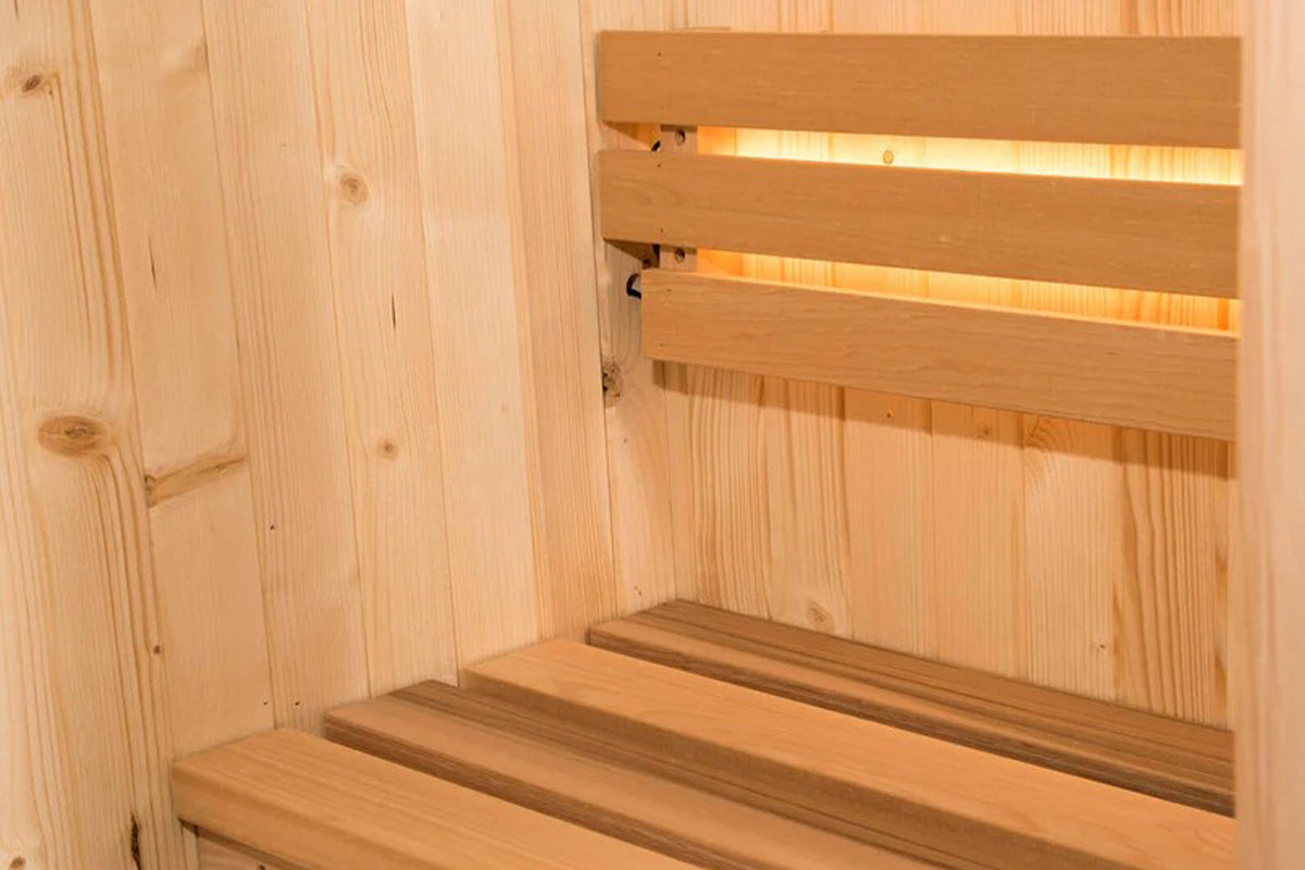 Interior view of wood sauna with tiered wooden benches and backrest, lit by integrated heating elements