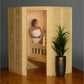 Light wood corner sauna with glass door, woman seated inside wrapped in white towel, potted plant beside sauna on wooden floo