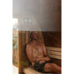 Man relaxing shirtless inside wooden barrel sauna with curved benches and glass door