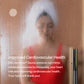 Person wearing white towel and red top in steamy sauna with glass door visible on right side