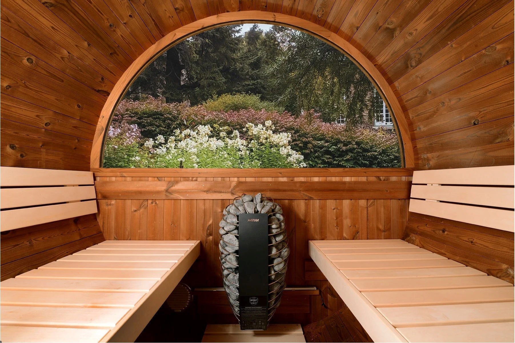 Cedar barrel sauna interior with half-moon arched window, wooden benches on both sides, and black heater with stone rocks, ga