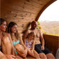Family of four relaxing inside wooden barrel sauna with mountain landscape view through window
