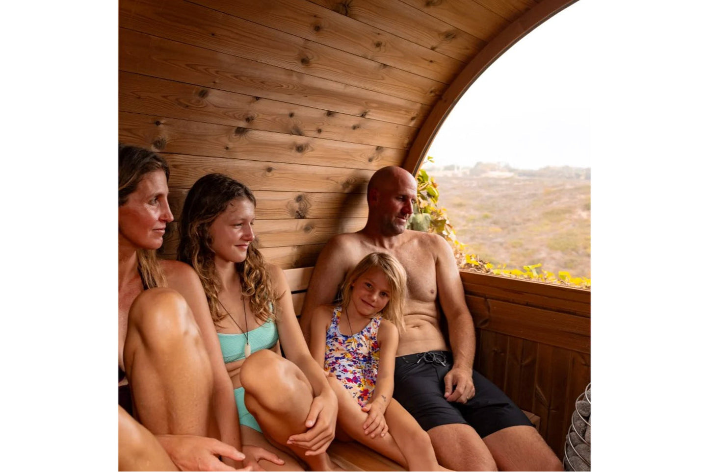 Family of four relaxing inside wooden barrel sauna with mountain landscape view through window