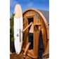White and wood surfboard leaning against wooden barrel sauna, man in black shorts entering sauna door, blue sky background