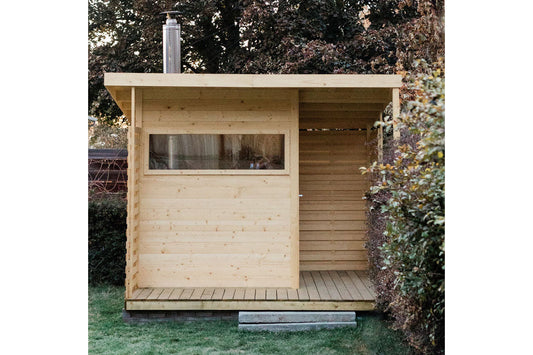 Natural pine wood sauna with large window, open right side, and metal chimney, positioned in backyard garden setting