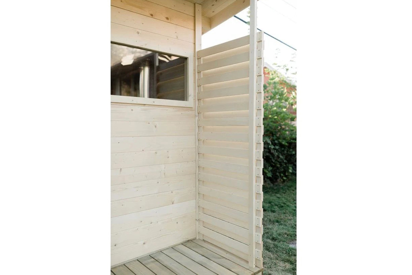 Natural wood sauna interior with horizontal siding, window, and louvered door panel in garden setting