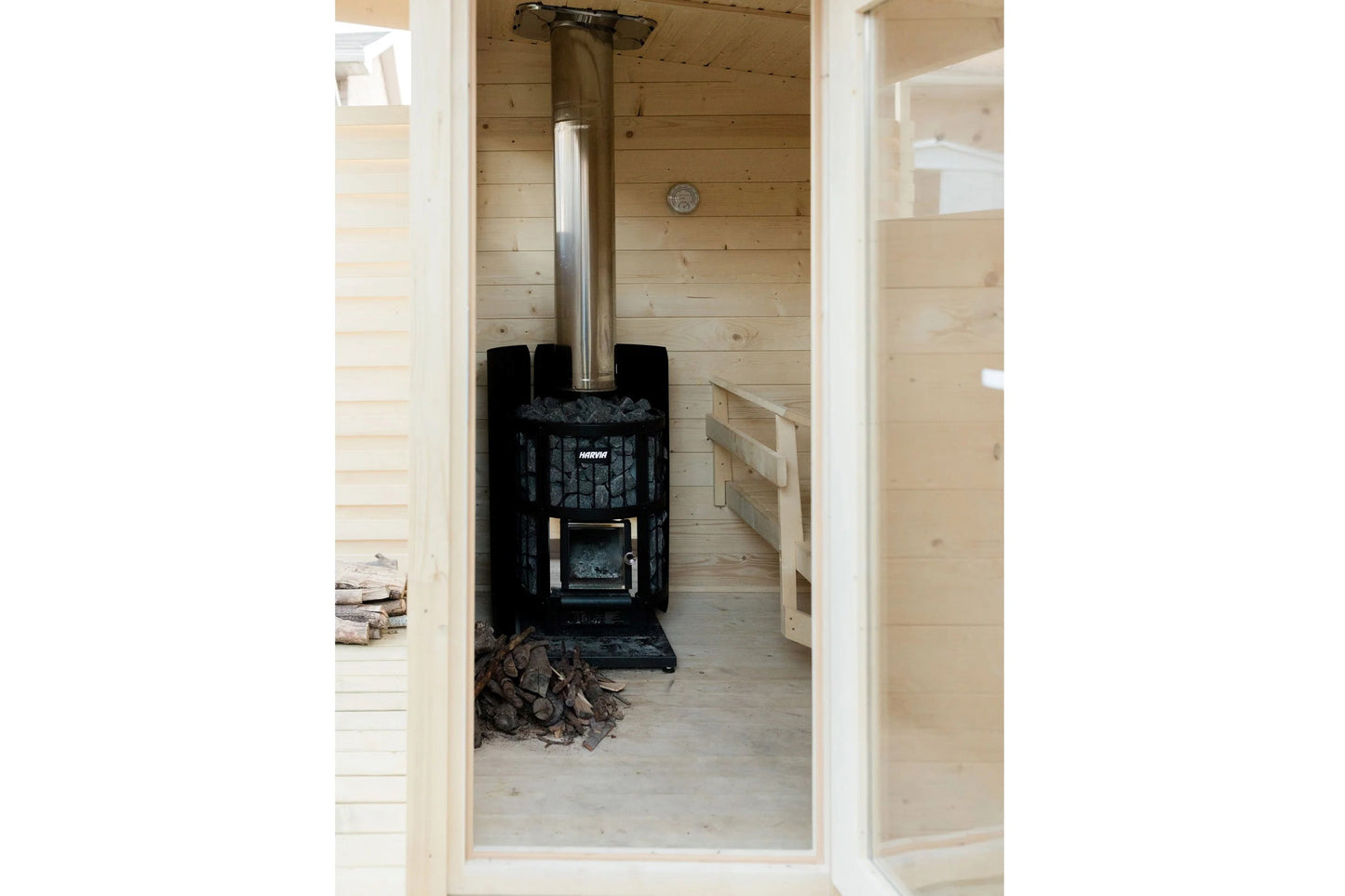Black wood-burning sauna stove with chimney inside light wood sauna cabin interior