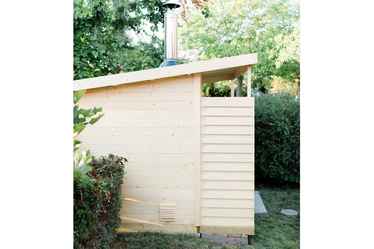 Cream-colored wooden sauna cabin with horizontal siding, louvered wall panel, and chimney pipe on roof, surrounded by green h