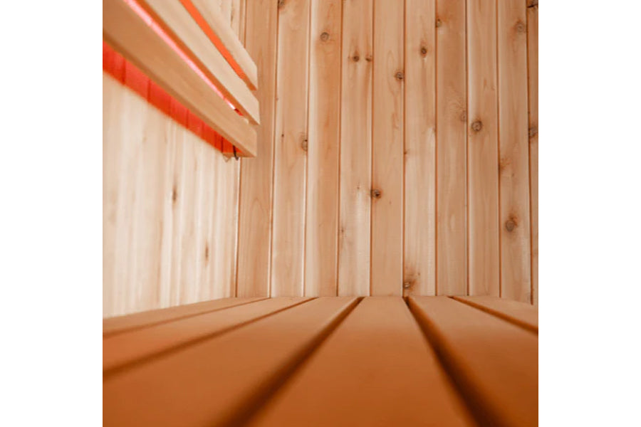 Interior view of wooden sauna with vertical pine paneling, orange bench seating, and heat lamp visible in upper left corner