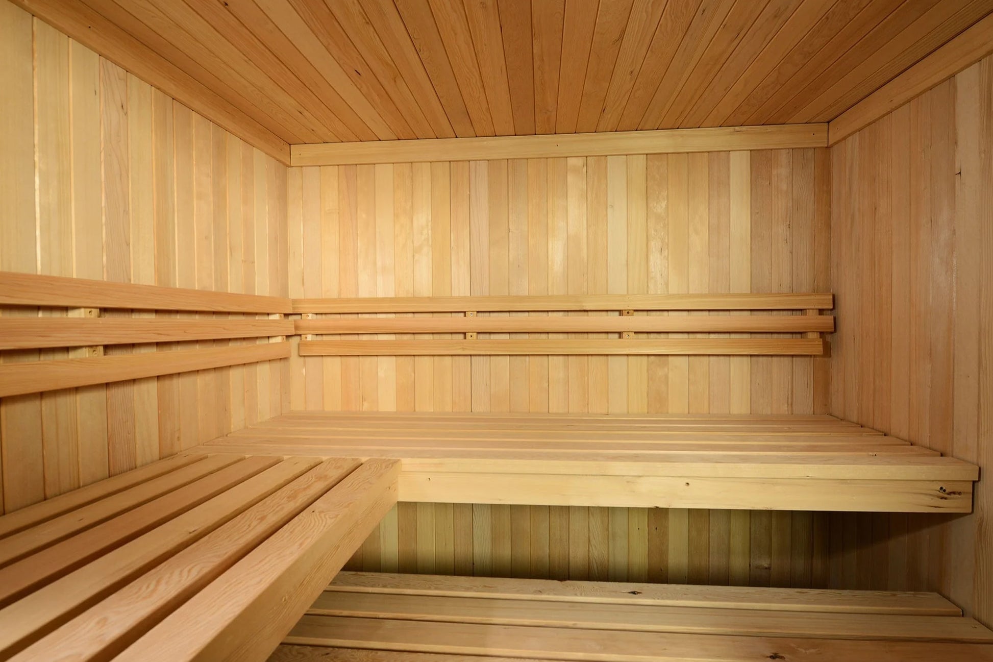 Interior view of wooden sauna with light pine bench seating, vertical and horizontal wood paneling, and two tiered benches fo