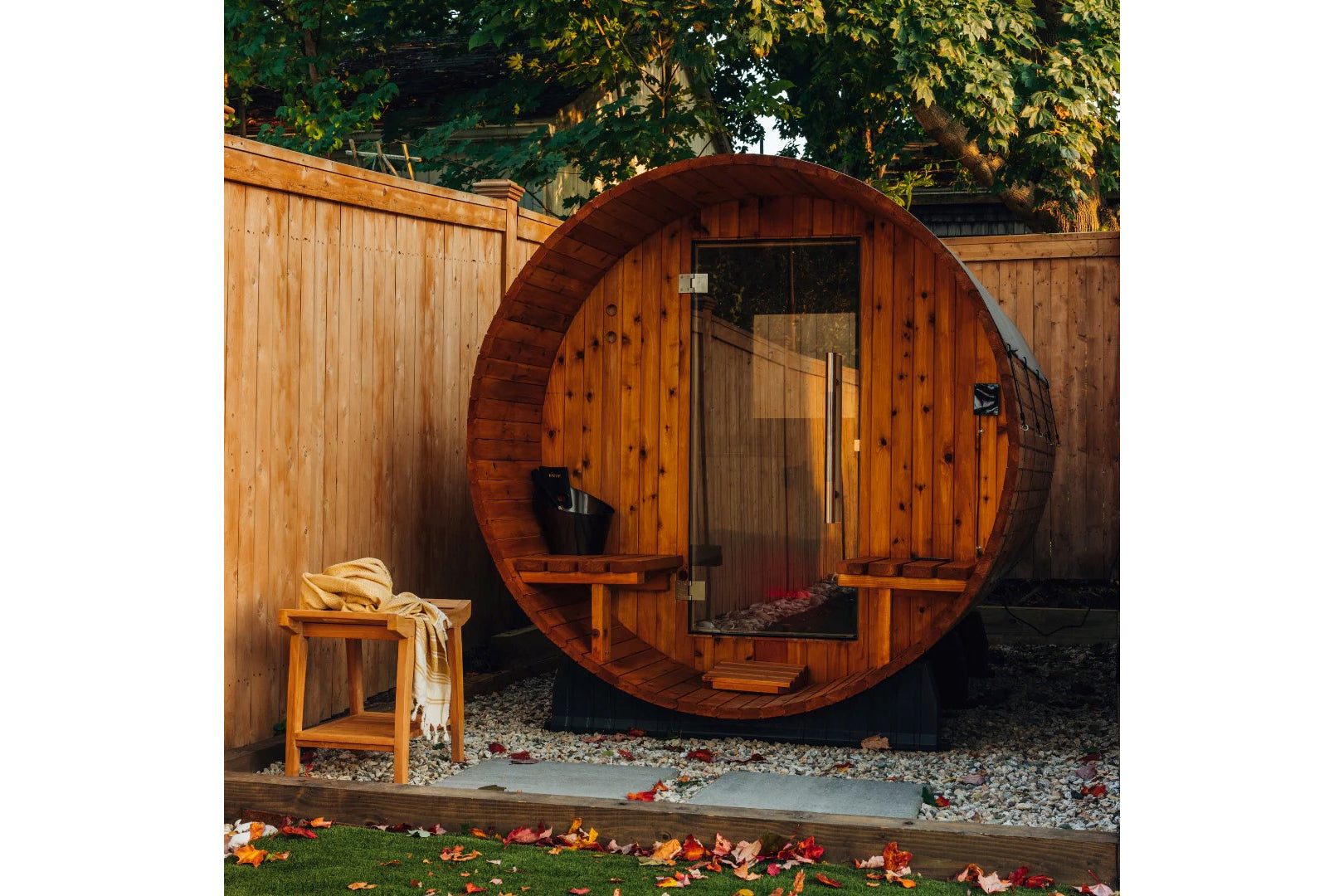 Barrel sauna with rounded wooden exterior, glass door, and wooden benches inside, situated in backyard garden setting with wo