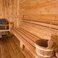 Interior of wooden sauna with benches, cedar walls, barrel heater, and wooden bucket on bench