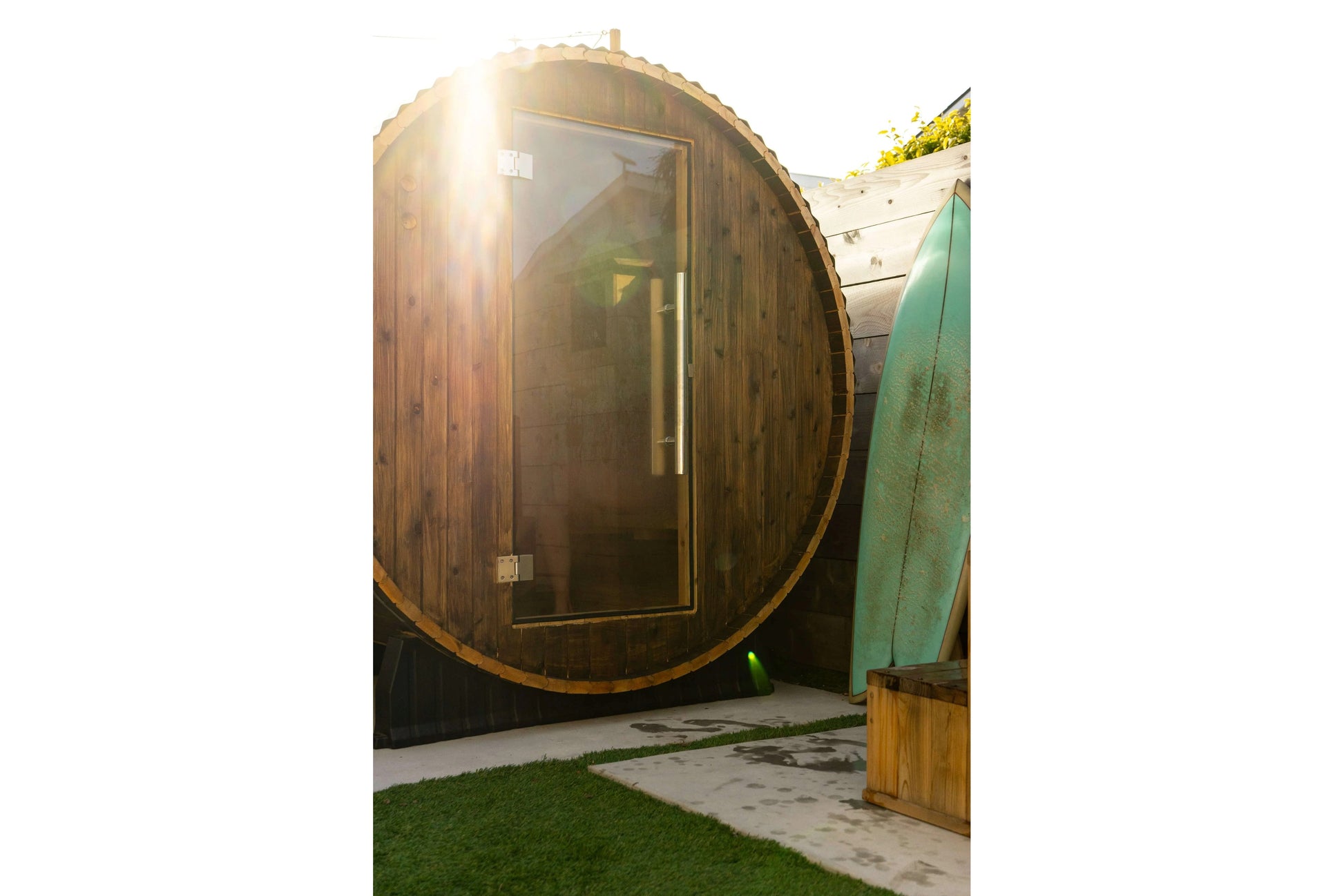 Watoga 4-person barrel sauna with dark wood exterior, glass door, and metal bands, positioned in outdoor garden setting