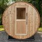 Natural wood barrel sauna with rounded cedar exterior, glass window, and wooden door with handle, displayed outdoors on grave