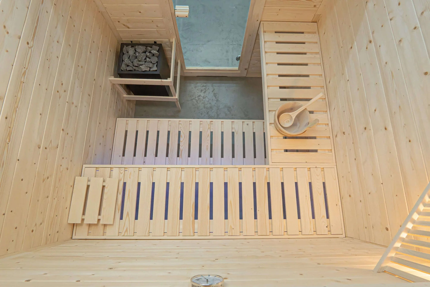 Interior overhead view of wooden sauna with pine walls, two benches with blue backrest supports, heater with gray stones, sky