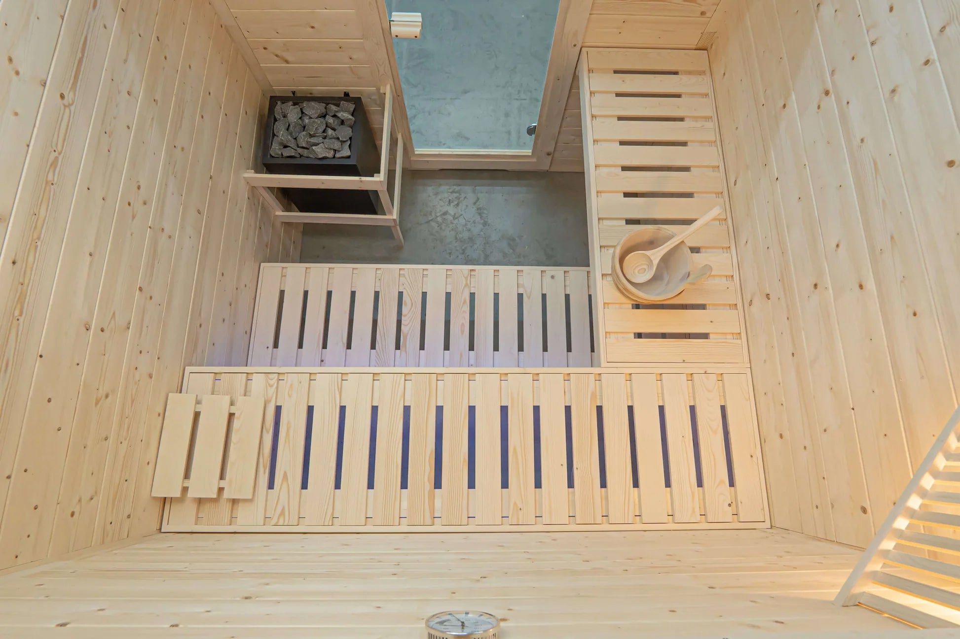 Interior overhead view of wooden sauna with pine walls, two benches with blue backrest supports, heater with gray stones, sky