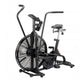Black air bike with large fan wheel, dual handles, padded seat, and foot pedals on white background