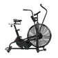 Black stationary air bike with large fan wheel, padded seat, dual handlebars, and resistance display on white background