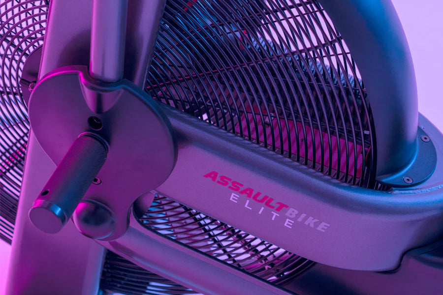 Assault Elite air bike with purple and blue gradient frame, black mesh fan cage, and control handles on purple background
