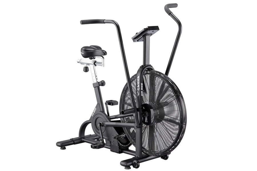 Black stationary air bike with large fan wheel, padded seat, dual handles, and foot pedals on white background