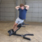Man wearing navy t-shirt and gray shorts using black 45-degree ab/back hyperextension bench in garage setting