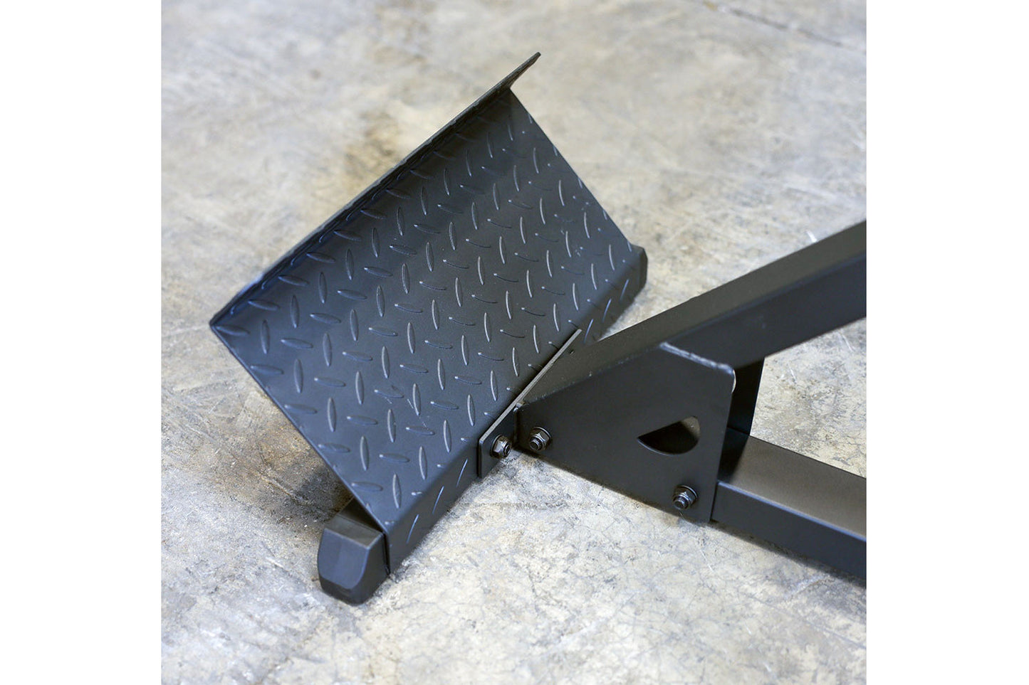 Black textured footplate attached to metal hyperextension machine frame on concrete surface