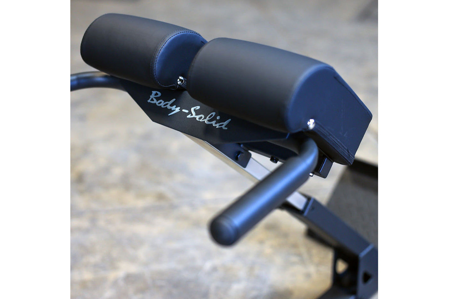 Body-Solid ab/back hyperextension machine with black and blue padded seat and backrest on stone surface