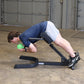 Person performing ab exercise on black Body-Solid hyperextension machine while holding green medicine ball in garage setting
