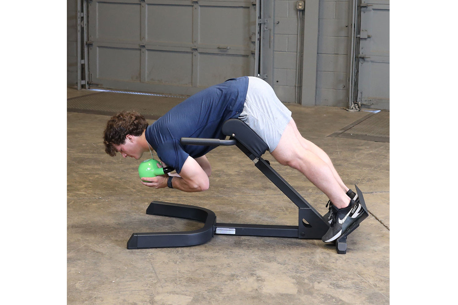 Person performing ab exercise on black Body-Solid hyperextension machine while holding green medicine ball in garage setting
