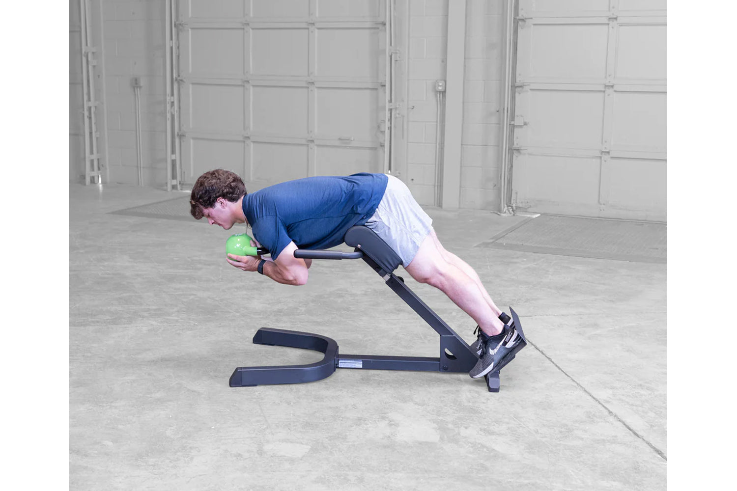 Man performing ab exercise on black hyperextension bench holding green medicine ball in garage setting