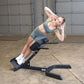 Woman performing ab crunch exercise on gray Body-Solid hyperextension bench in industrial gym setting