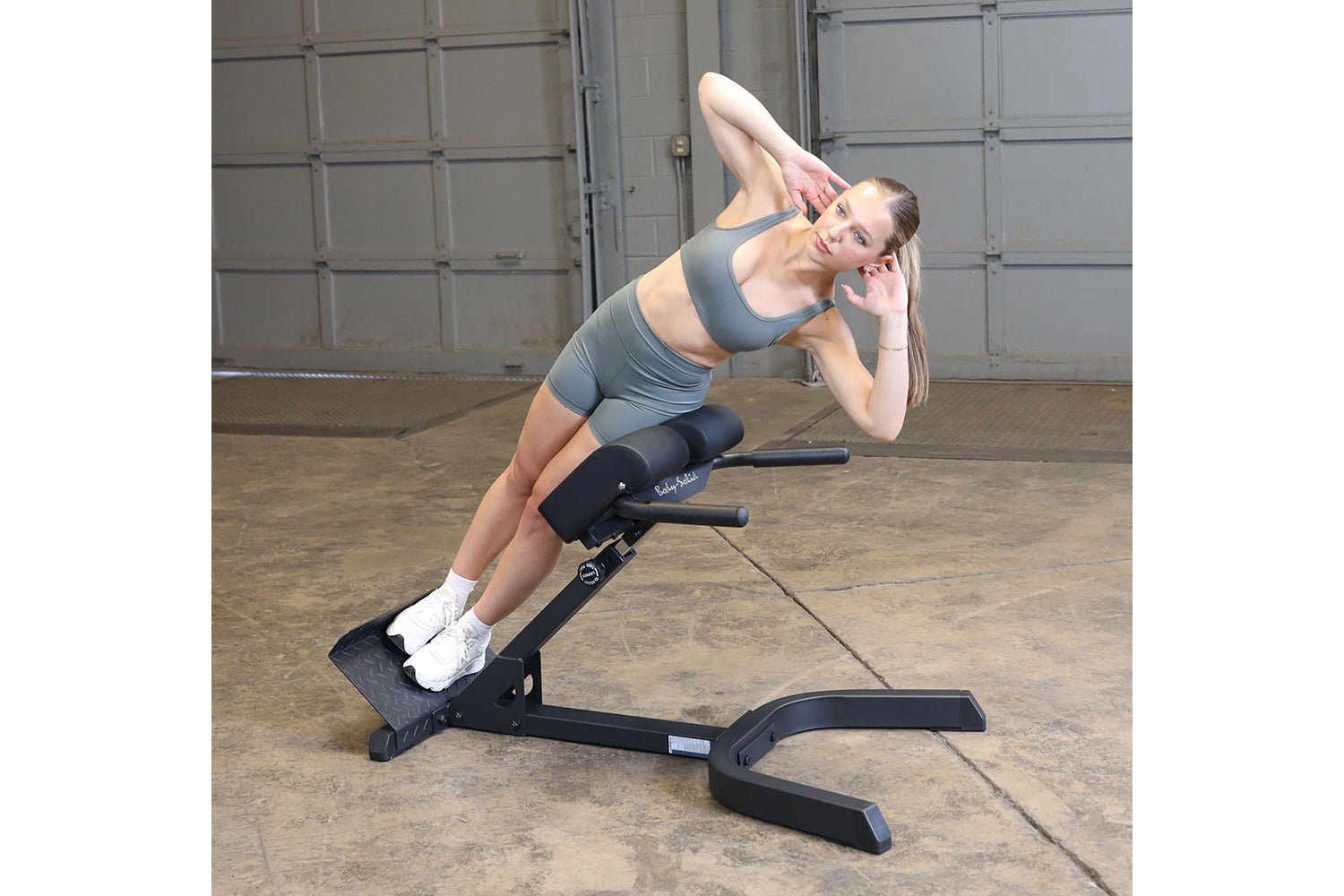 Woman performing ab crunch exercise on gray Body-Solid hyperextension bench in industrial gym setting