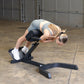 Woman using black Body-Solid hyperextension bench in 45-degree ab/back exercise position in warehouse setting