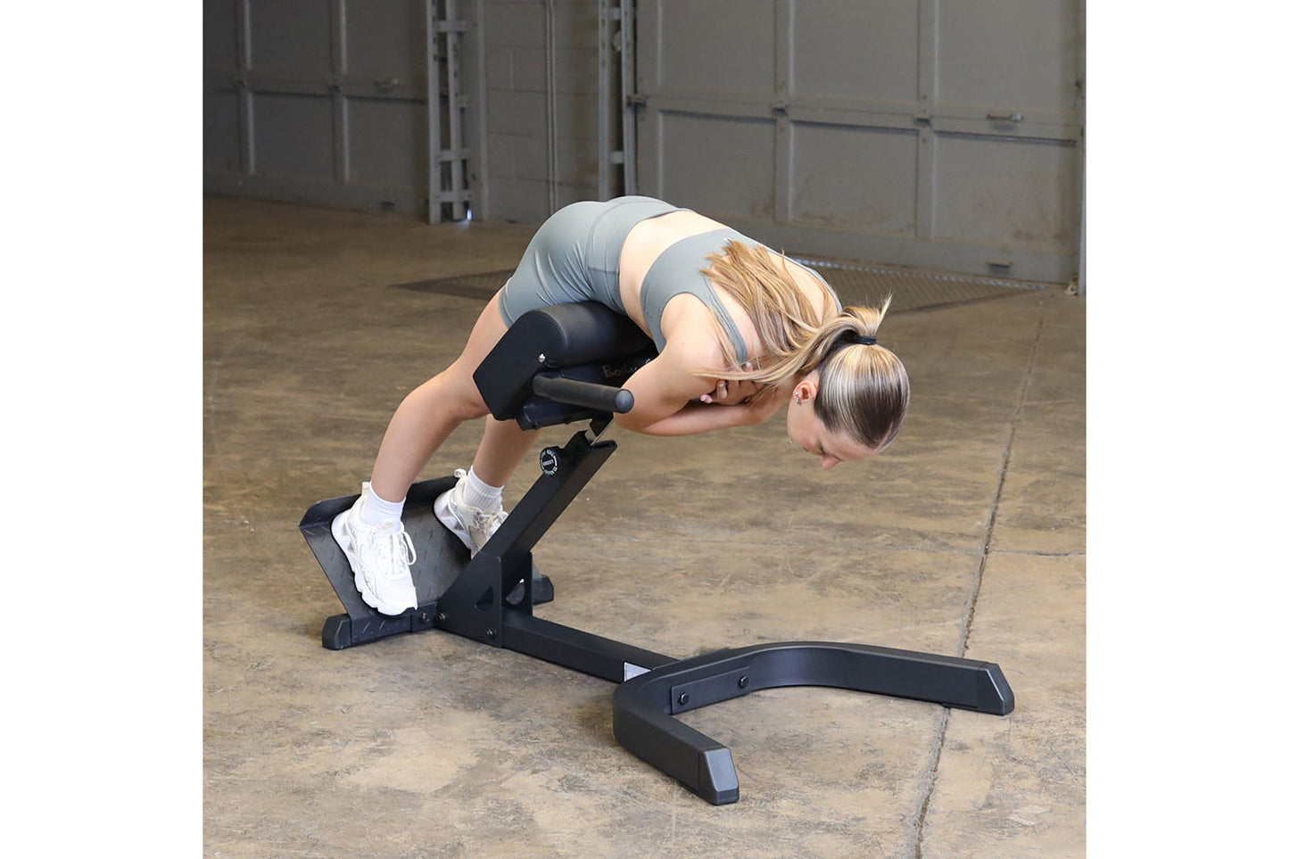 Woman using black Body-Solid hyperextension bench in 45-degree ab/back exercise position in warehouse setting