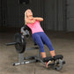 Woman performing ab exercise on Body-Solid weight bench machine, wearing pink tank top and navy capri leggings in gym setting
