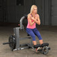 Woman wearing hot pink sleeveless tank and navy capri leggings using gray and black ab and back exercise machine in gym setti
